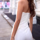 Woman wearing a white strapless jumpsuit on a city street.