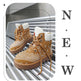 A pair of tan lace-up ankle boots with white bandana paisley prints on the sides, white faux-fur collars, and brown soles, displayed on a metallic roller conveyor. The image has a stylized border and the text 'NEW' printed vertically on the right.