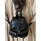 Black leather backpack worn over a beige coat