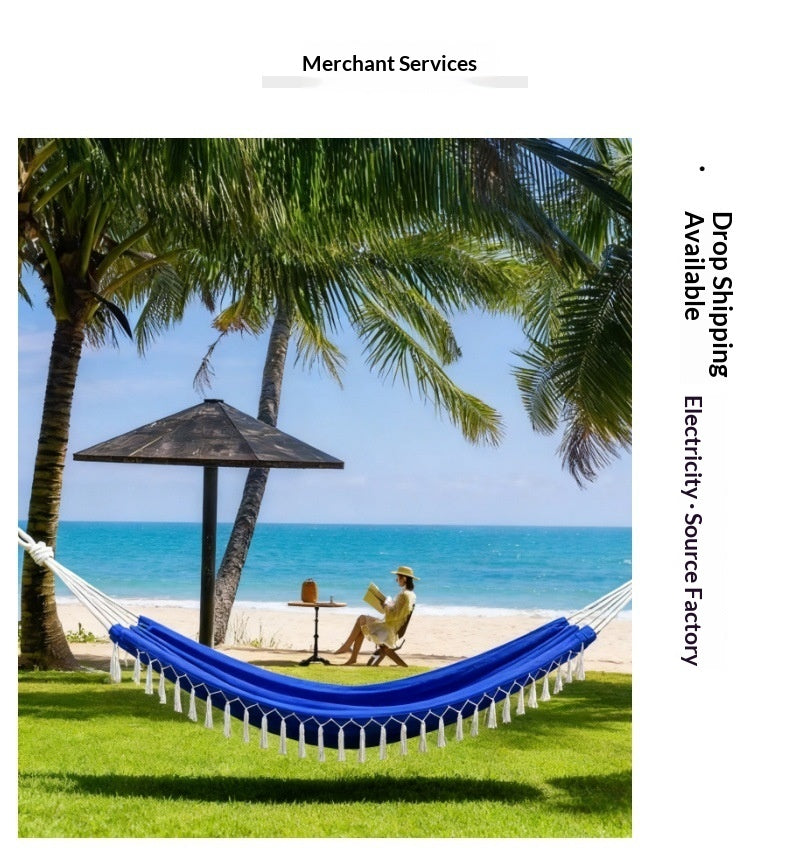 A blue and white woven hammock strung between palm trees on a grassy lawn, with a beach, ocean, and seated person visible in the background. Text on the right reads 'Drop Shipping Electricity-Source Factory' and 'Merchant Services' appears at the top.
