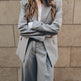 Person wearing a gray suit standing against a beige wall.