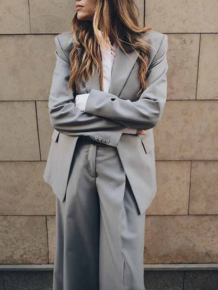 Person wearing a gray suit standing against a beige wall.