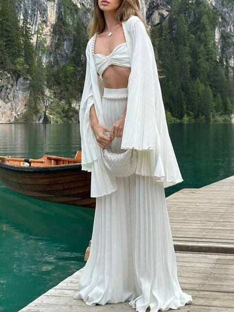 Woman in a white outfit standing on a dock by a lake with mountains in the background
