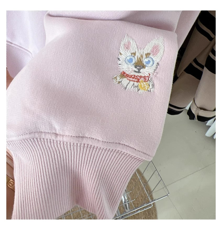 Pink sweater with embroidered cat design on a chair.