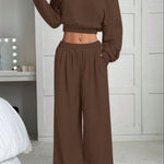 Person wearing a brown off-shoulder top and wide-leg pants in a bedroom setting.