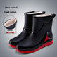 Black rain boots with red soles on a gray background