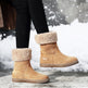 Tan winter boots with fur trim worn by a person on a snowy ground.