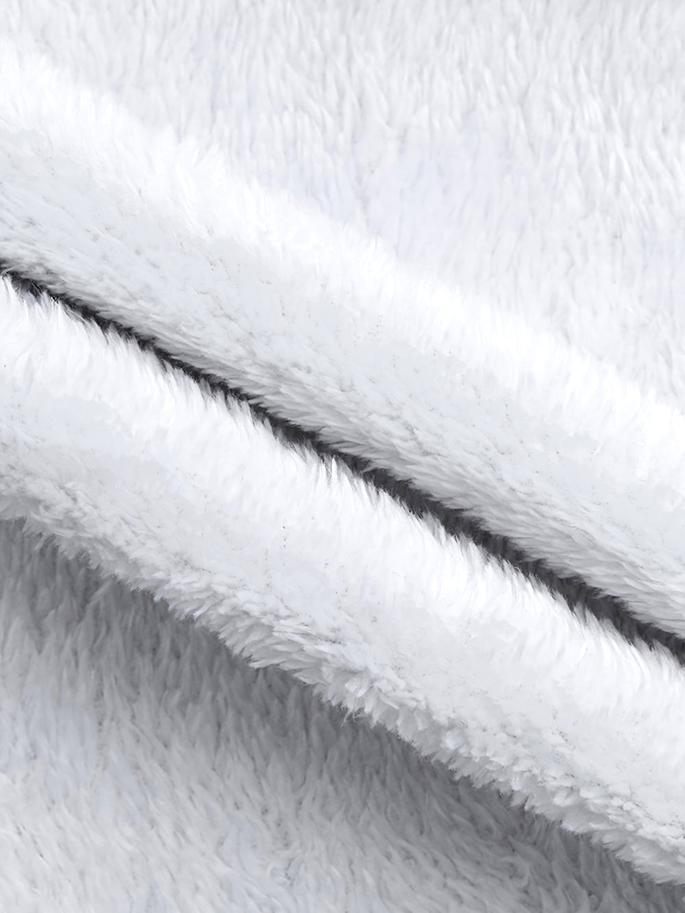Close-up of a soft white plush or sherpa fabric with folded layers showing the fuzzy texture and a dark center seam.
