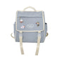 Sac à dos gris avec des patchs de personnages de dessin animé sur fond blanc.