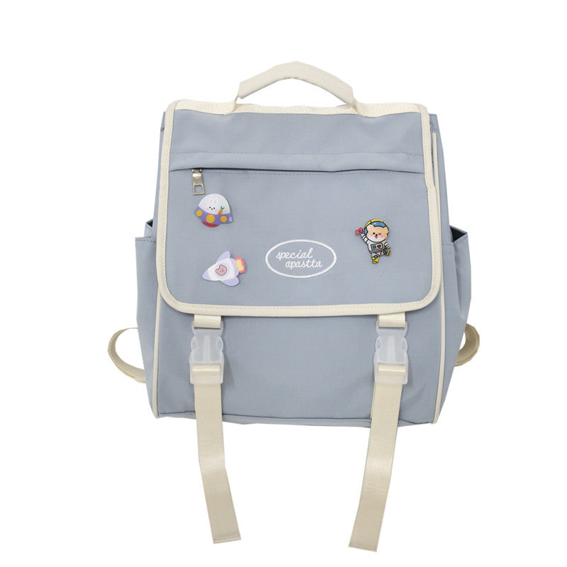 Sac à dos gris avec des patchs de personnages de dessin animé sur fond blanc.