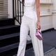 Woman in a white strapless jumpsuit holding a pink clutch on a city street.