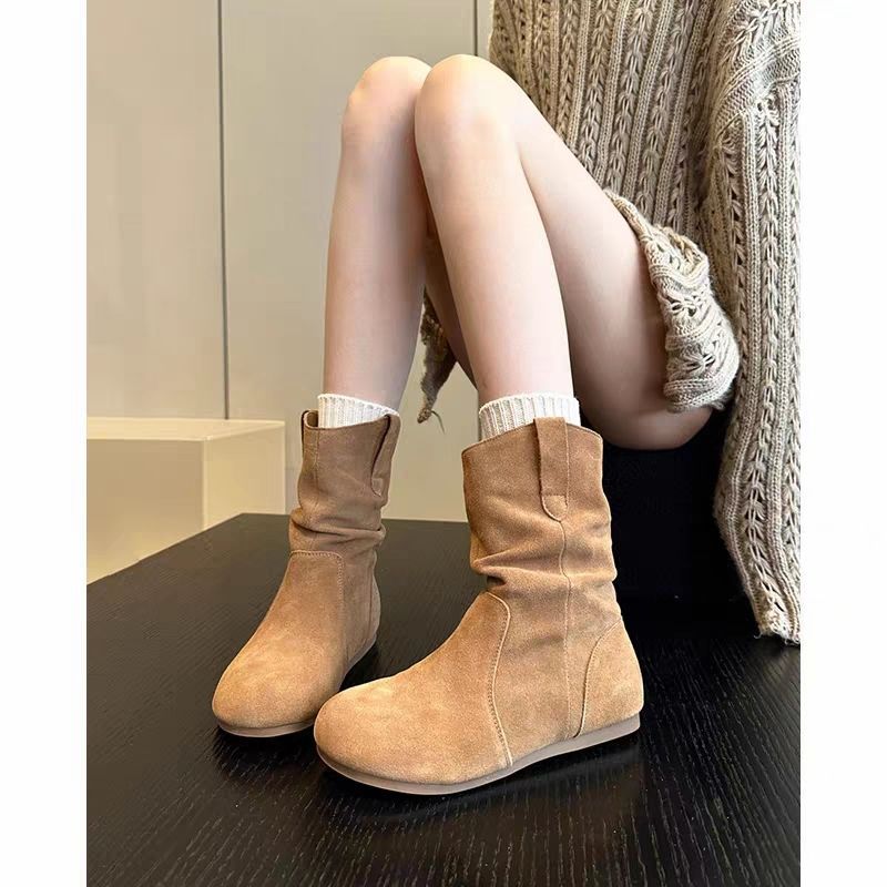 Tan suede boots worn by a person sitting on a dark surface with a neutral background