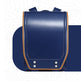 A navy blue leather school backpack with tan leather trim and silver metal rivets, shown from a front-facing perspective on a stylized white background.