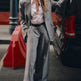 Woman in a gray suit standing next to a black car on a city street.
