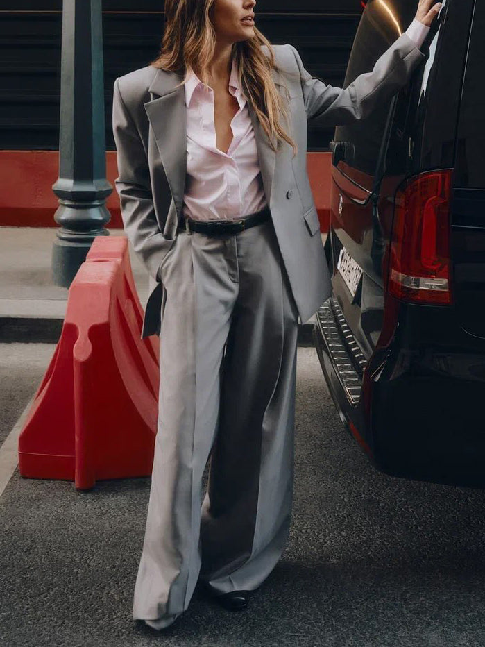 Woman in a gray suit standing next to a black car on a city street.