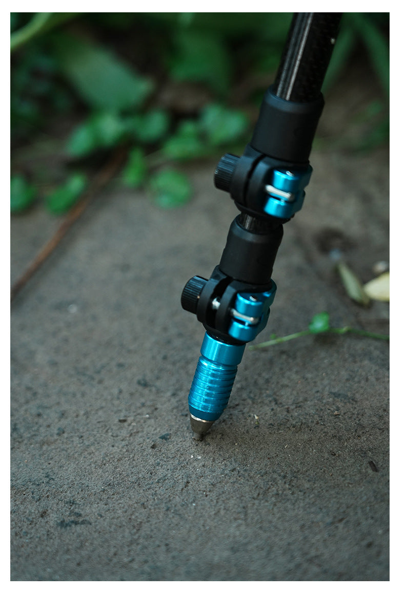 Close-up of a fishing rod section with black and bright blue anodized aluminum joints, standing on concrete outdoors with blurred green foliage in the background.