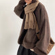 Person wearing a brown sweater and scarf with a matching bag on a white background