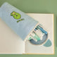 Pencil case with stationery items on a notebook against a green background