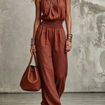 Woman wearing a rust-colored jumpsuit holding a matching handbag against a neutral background