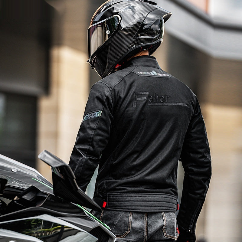 Person wearing a black motorcycle jacket and helmet standing next to a motorcycle.