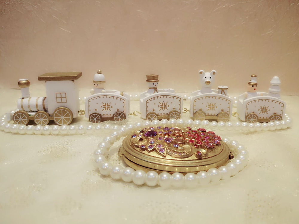 Decorative train set with small bears on a beige background, surrounded by pearls and jewelry.