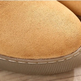 Close-up of a tan suede slipper or boot toe with a textured gray sole, resting on a light wood surface.
