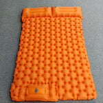 An orange inflatable camping sleeping pad with a honeycomb bubble design, laid flat on a gray textured surface.