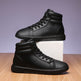 Pair of black high-top sneakers on a wooden surface with a light purple background