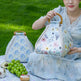 Woman holding a floral-patterned bag outdoors with green grass in the background