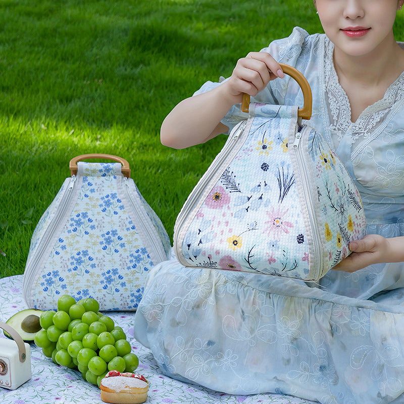 Woman holding a floral-patterned bag outdoors with green grass in the background