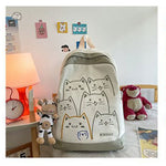 Backpack with cat designs on a bed with toys and a lamp in the background