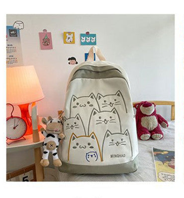 Backpack with cat designs on a bed with toys and a lamp in the background