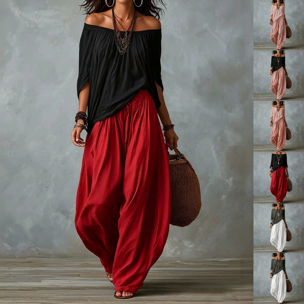 A woman models a loose off-the-shoulder black top with voluminous red wide-leg pants, standing against a textured gray wall. A vertical strip on the right shows the same outfit in several other colors.