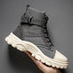 Gray tactical boot with beige sole held by a hand on a gray background