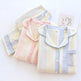 Three folded long-sleeve pajama shirts in pastel striped colors are arranged on a white background. The front shirt is cream, light blue, and lavender, with a light blue piping collar.