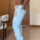 Person wearing light blue distressed jeans and a white top in an indoor setting.