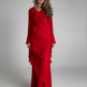 A woman modeling a long-sleeved red dress with cascading ruffle details, standing against a neutral light gray studio background.
