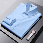 Folded light blue dress shirt with a white watch on a gray surface